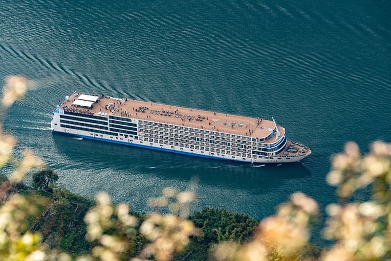 A Century vessel seen from directly above, cutting a wake across jade-green water