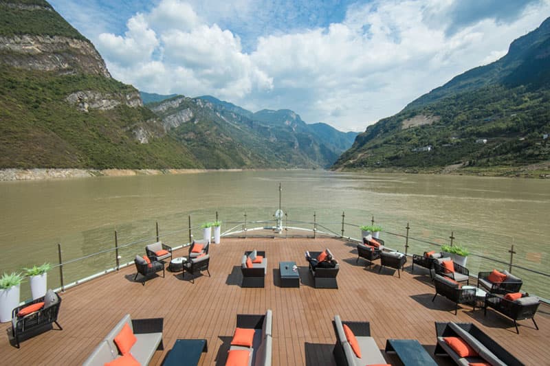 Teak sun deck with loungers under a wide sky, gorge walls rising on both sides