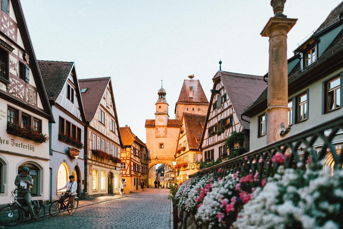 A cobbled street of timber-framed houses running to a medieval gate tower at dusk