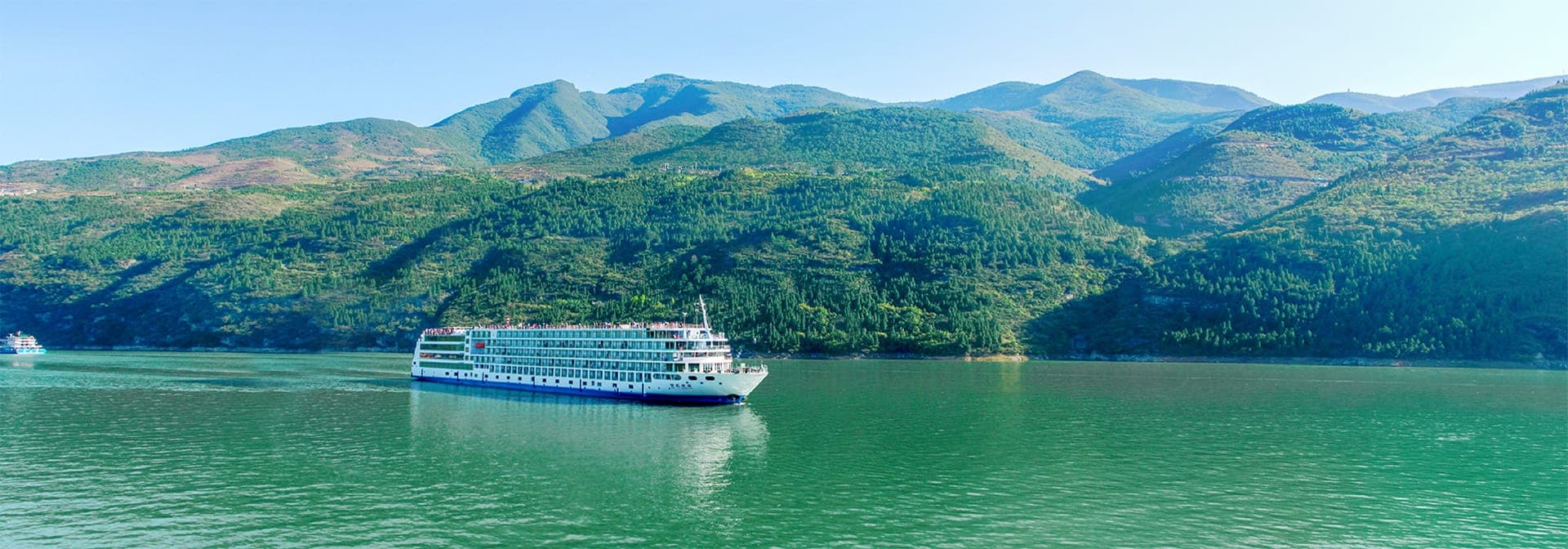 A river cruise vessel on jade-green water between steep forested mountains