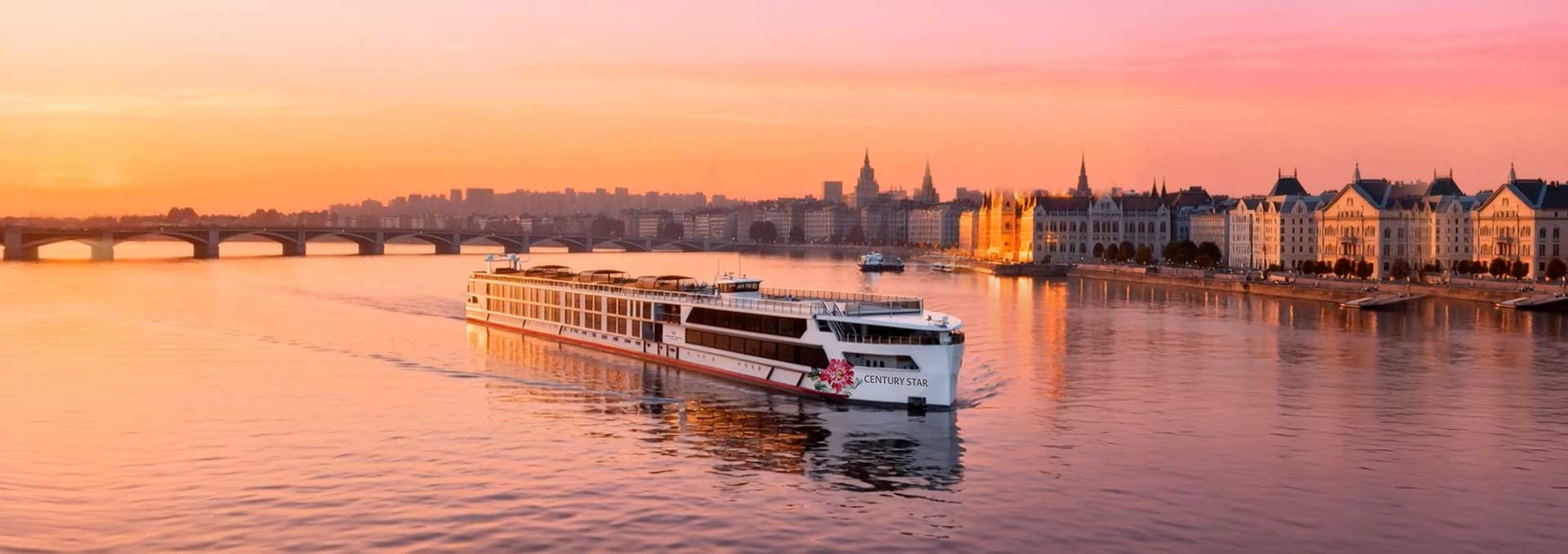 A river cruise vessel under way at sunrise, a bridge and a lit stone embankment behind her