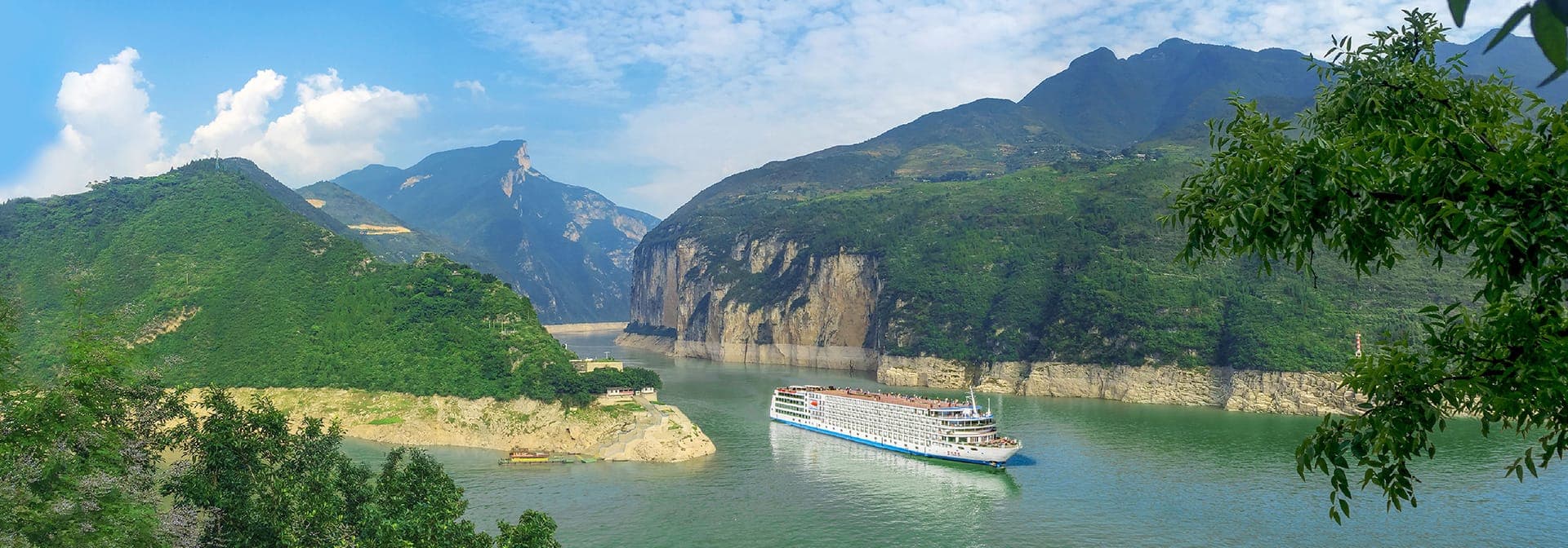 A river cruise vessel passing between gorge cliffs, seen through overhanging leaves