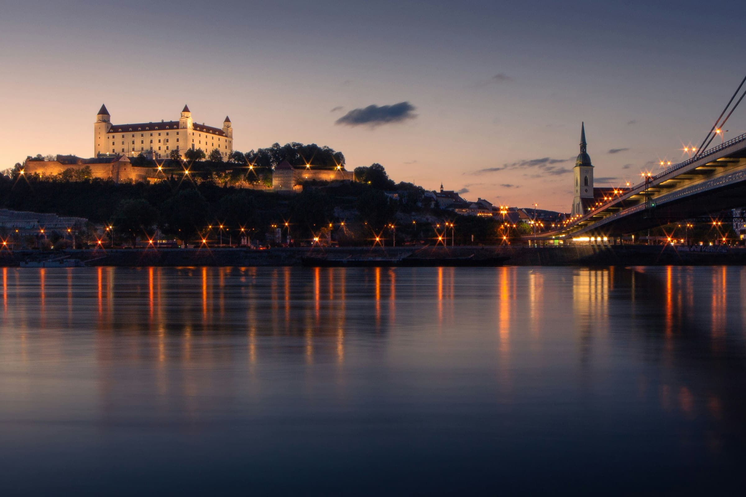 Bratislava castle above the Danube at dusk, the city lights carried on the water