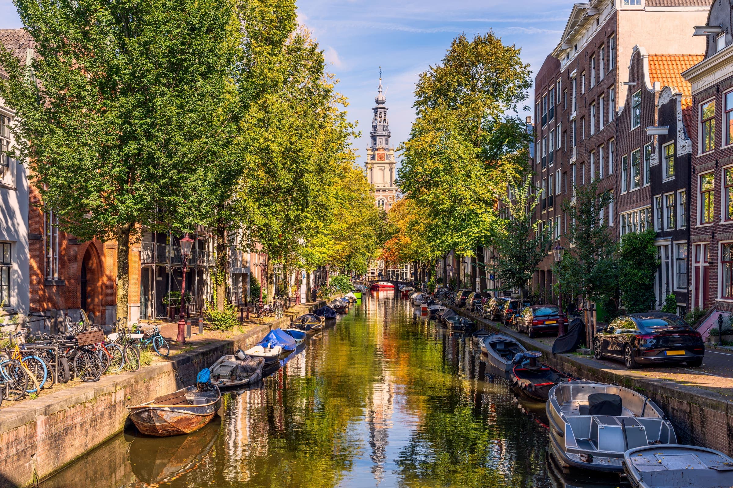 An Amsterdam canal in autumn, moored boats under the trees and gabled houses beyond